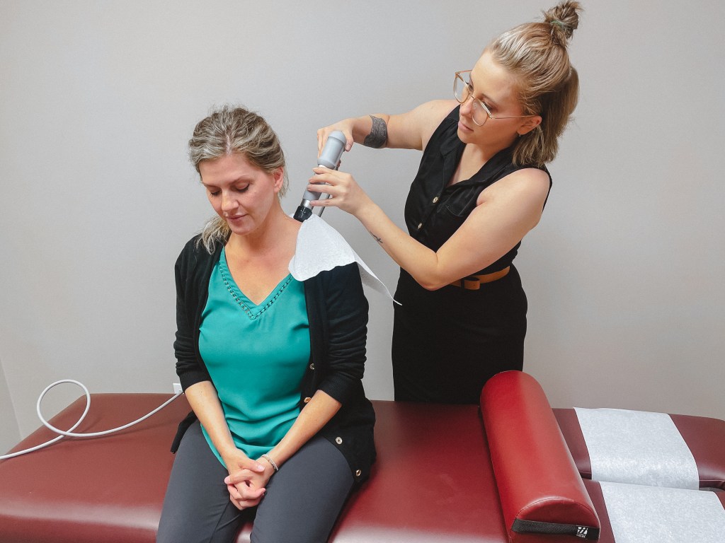 patient sitting down receiving shockwave therapy by doctor for shoulder pain